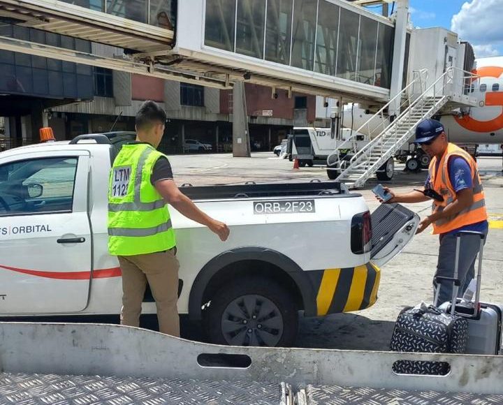 Operadores cargando maletas en una camioneta junto a una manga del aeropuerto