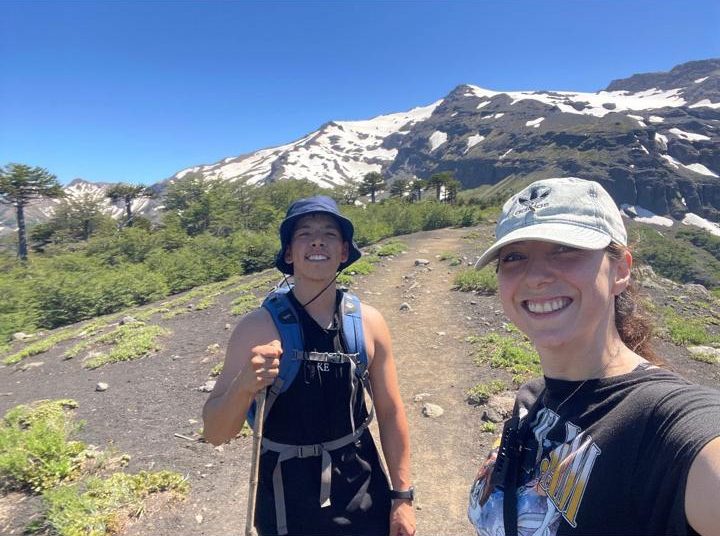 Álvaro y Valeria de trekking entre araucarias, con un volcán nevado al fondo